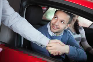 Man shaking the hand of a car dealer while sitting on a car.jpeg